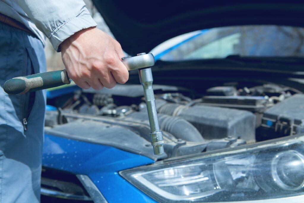 Hand holding a socket wrench over the open engine bay of a car during scheduled maintenance