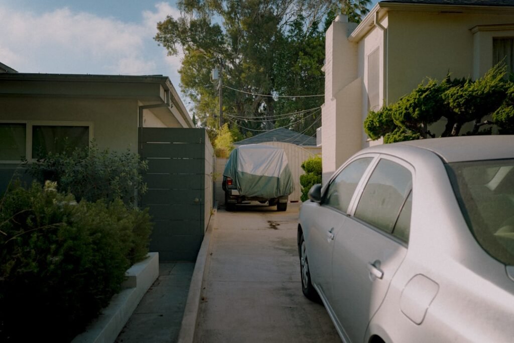 A covered work vehicle and an everyday sedan sharing a narrow home driveway — two cars, two separate choices between the ATO logbook method and cents per kilometre